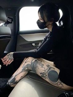 a woman sitting in the back seat of a car with tattoos on her legs and arms