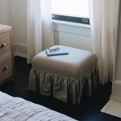 a bed sitting under a window next to a white dresser with a book on it