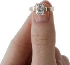 a woman's hand holding an engagement ring with a square diamond in the middle