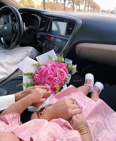 two people sitting in a car with flowers on the floor and one person holding hands