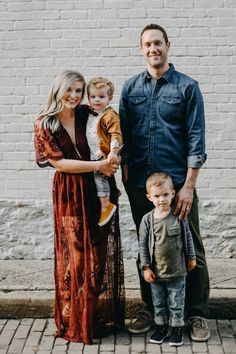 a man, woman and child standing in front of a white brick wall with their arms around each other