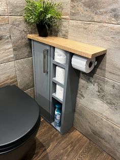 a toilet and cabinet in a bathroom with wood flooring next to a potted plant