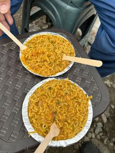 two paper plates with noodles and chopsticks in them sitting on an outdoor table