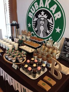 a table topped with lots of cupcakes and cakes next to a starbucks sign