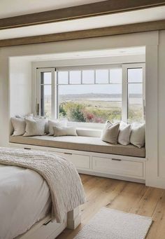 a bedroom with a large window seat next to a white bed and wooden flooring