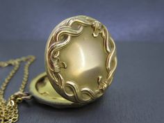 "Lovely antique locket set with an ornate design.  Opens and closes with a snap.  Nice and thick locket, well made. No frames/covers inside and some patina inside.  A little patina on the outside, some wear to the finish, and some very tiny dings.  Comes with a brand new 18\" gold plated stainless steel chain. All items added to your cart at Ribbons Edge will automatically combine shipping. To stay up to date with my newest offerings, follow me on IG @ RibbonsEdge" Ornate Medallion Locket Necklace With Vintage Charm, Antique Gold Medallion Locket Necklace With Vintage Charm, Antique Gold Medallion Locket Necklace, Antique Gold Brass Locket Necklace With Filigree, Antique Bronze Locket Necklace With Round Pendant, Antique Bronze Round Locket Necklace, Antique Bronze Round Pendant Locket Necklace, Heirloom Antique Gold Locket Necklace With Antique Finish, Ornate Bronze Locket Necklace In Brass