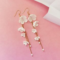 two pairs of earrings with white flowers and pearls hanging from them on a pink surface