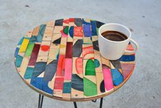 a cup of coffee sitting on top of a wooden table covered in multicolored tiles