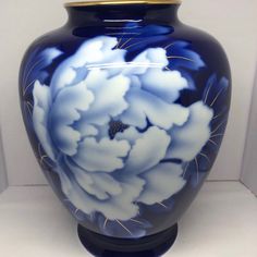 a blue vase with white flowers painted on the side and gold rimmed lid sitting in front of a white wall