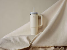 a white cup sitting on top of a bed under a blanket