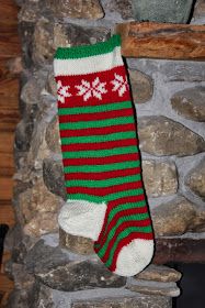 a green and red striped sock hanging from a stone fireplace mantel with logs in the background