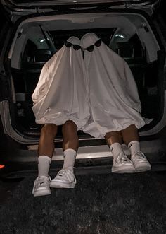 two people in white outfits sitting on the back of a car with their feet up