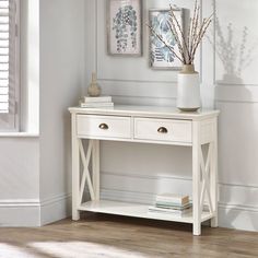 a white table with two drawers and a vase on it in front of a window