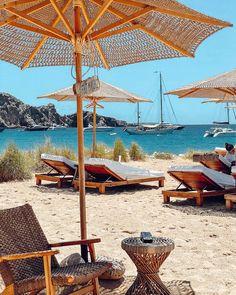 lounge chairs and umbrellas on the beach with boats in the water