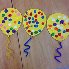 three paper plates with balloons and streamers on them sitting on a wooden floor next to a pair of scissors