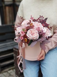 a woman holding a pink flower box with flowers in it's lap and wearing jeans