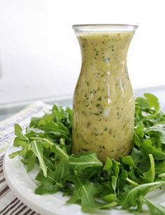 a white plate topped with lettuce next to a small glass bottle filled with dressing