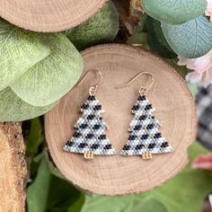 two triangle shaped beaded earrings sitting on top of a piece of wood next to flowers