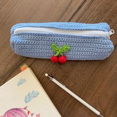 a crocheted pencil case with a cherry on it and a book next to it