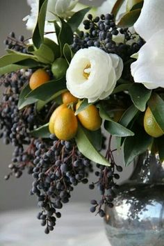 a vase filled with white flowers and oranges on top of a table next to a wall