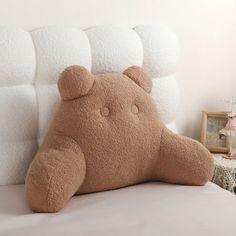 a brown teddy bear sitting on top of a bed next to a white headboard