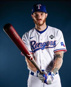 a baseball player holding a bat and posing for a photo in front of a blue background