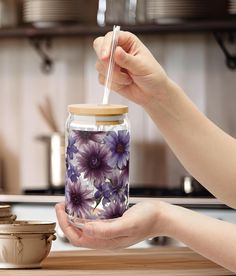 a person holding a jar with purple flowers on it and a straw in one hand