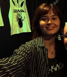 a man and woman posing for a photo in front of shirts hanging on the wall