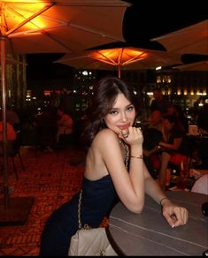 a woman sitting at a table with an umbrella over her head in the evening time