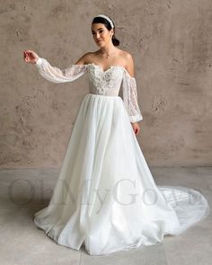 a woman in a white wedding dress with long sleeves and an off the shoulder top