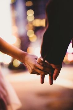 two people holding hands while standing on the street