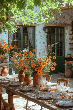 an outdoor dining table set with plates and vases filled with orange flowers on it