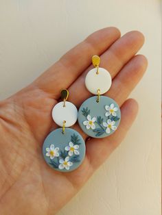 three white and blue flowers are hanging from the back of two round shaped dangles