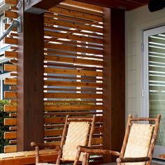 two wooden rocking chairs sitting on top of a patio next to a building with windows