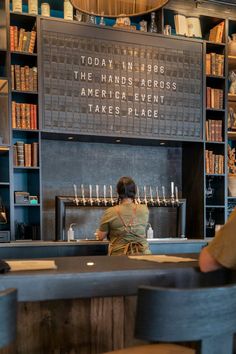 a woman sitting at a bar in front of a book shelf filled with lots of books