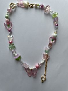 Embrace the whimsical charm of our Fairycore Butterfly Necklace! This handmade beaded necklace features a delightful mix of pink and green beads, adorned with butterflies, hearts, and flowers. Perfect for adding a touch of fairycore and kawaii style to any outfit, this necklace is a must-have for those who love unique and playful jewelry. Ideal for personal use or as a thoughtful gift, this necklace is designed to bring joy and enchantment to your accessory collection. The intricate beadwork and Cute Pink Beaded Chain Jewelry, Cute Handmade Green Beaded Necklaces, Cute Butterfly Necklace For Gift, Pink Beaded Charm Necklaces With Round Beads, Pink Beaded Charm Necklace With Round Beads, Whimsical Heart-shaped Beaded Necklace, Pink Kawaii Jewelry With Colorful Beads, Pink Round Beads Kawaii Jewelry, Pink Handmade Fairy Kei Jewelry