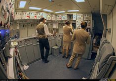 two men in tan suits are looking at the control panel on an airplane, while another man is standing next to them