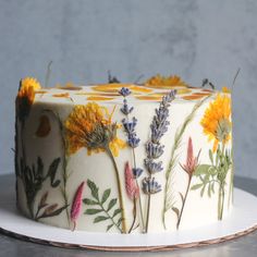 a cake decorated with wildflowers and other flowers sits on a white platter