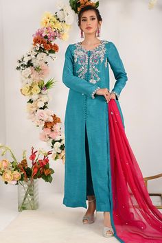 Steal the look this Eid by flaunting in our rosined which has intricate sitara floral embroidery followed with silver dabka, kora, water droplet pearls fine katdana and crystal work on neckline enhance with front open button down styled long silhouette shirt paired with vibrant fuchsine dupatta and straight pants. Shirt Fabric: Raw silk Shirt Length: 52” (customizable) Pant Fabric: Raw silk Dupatta Fabric: khadi net Shirt Color: teal blue Pant color: teal blue Dupatta Color: fuchsine All outfits Elegant Lawn Suit With Dabka For Festivals, Elegant Lawn Suit With Dabka Detail For Transitional Season, Elegant Chinon Sharara With Dabka Detail, Eid Raw Silk Lawn Suit With Mirror Work, Formal Dabka Kurta In Chinon, Eid Lawn Suit In Raw Silk With Mirror Work, Party Traditional Wear In Cotton Silk With Dabka, Festive Chinon Lawn Suit With Mirror Work, Party Traditional Wear With Dabka On Cotton Silk