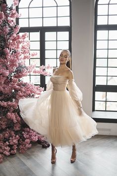 a woman in a white dress standing next to a tree with pink flowers on it