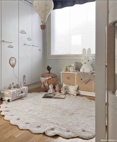 a room with white walls and wooden floors has stuffed animals on the floor, bookshelves in the background