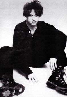 a young man sitting on the ground with his feet up next to two pairs of shoes