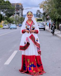 a woman in a white and red dress is standing on the side of the road