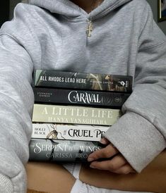 a person wearing a gray hoodie holding several books in their hands while sitting down