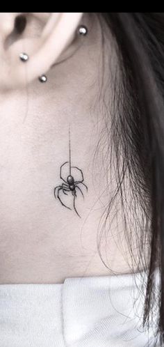 a woman's neck with a spider tattoo on the back of her left shoulder