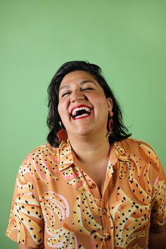 a woman is laughing while wearing an orange shirt and red earrings with her eyes closed