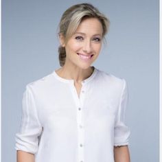 a woman with blonde hair wearing a white shirt and smiling at the camera while standing in front of a gray background