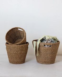 A still life image features two Round Woven Baskets by Creative Co-op placed against a plain white background. The basket on the left is empty with another basket nested inside it, showcasing their natural charm. The basket on the right contains rumpled, colorful fabric with green and white striped material on top, emphasizing an eco-friendly aesthetic. Ikea Jute Basket, Road Trip Gifts, Seagrass Baskets, Grass Basket, Towel Organization, Seagrass Basket, Hand Woven Baskets, Basket Set, Home Goods Decor