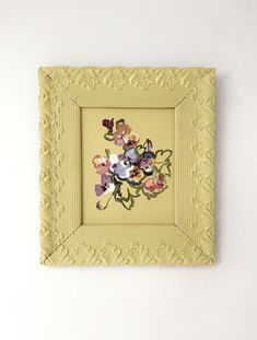 a yellow frame with flowers painted on the inside is hanging on a wall in front of a white wall