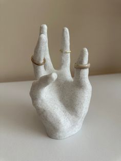 a white ceramic hand with gold rings on it's thumb and ring holder in the shape of a peace sign